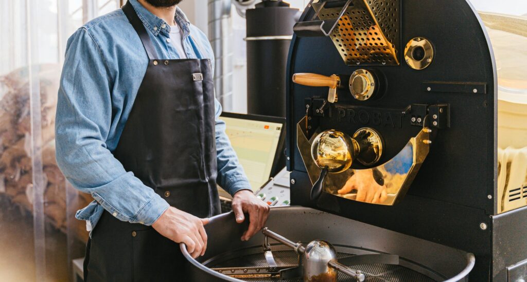 Bearded man working with a coffee roaster in a modern workshop. Indoor setting.